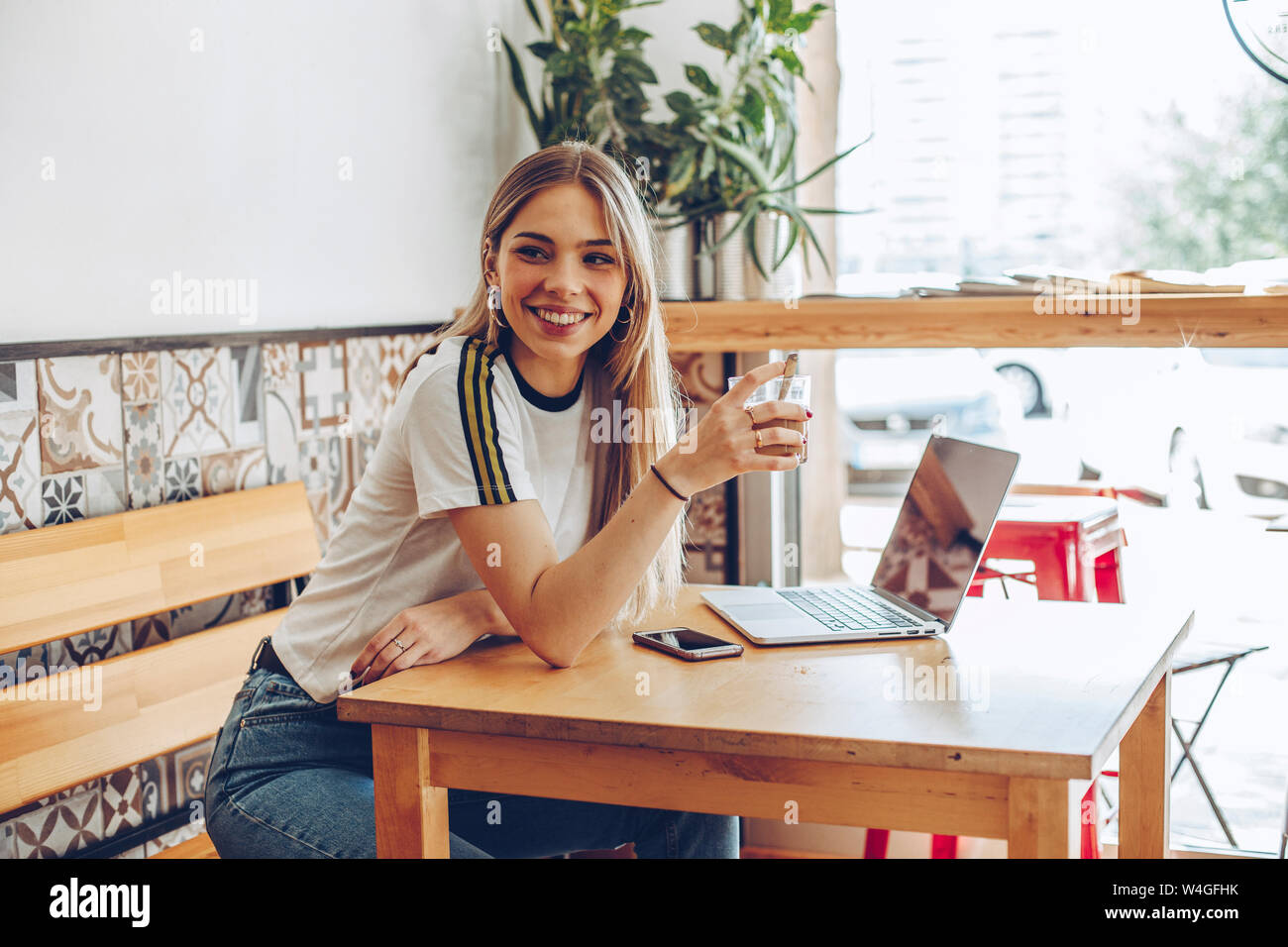 Junge Frau mit dem Handy und dem Laptop im Cafe Stockfoto