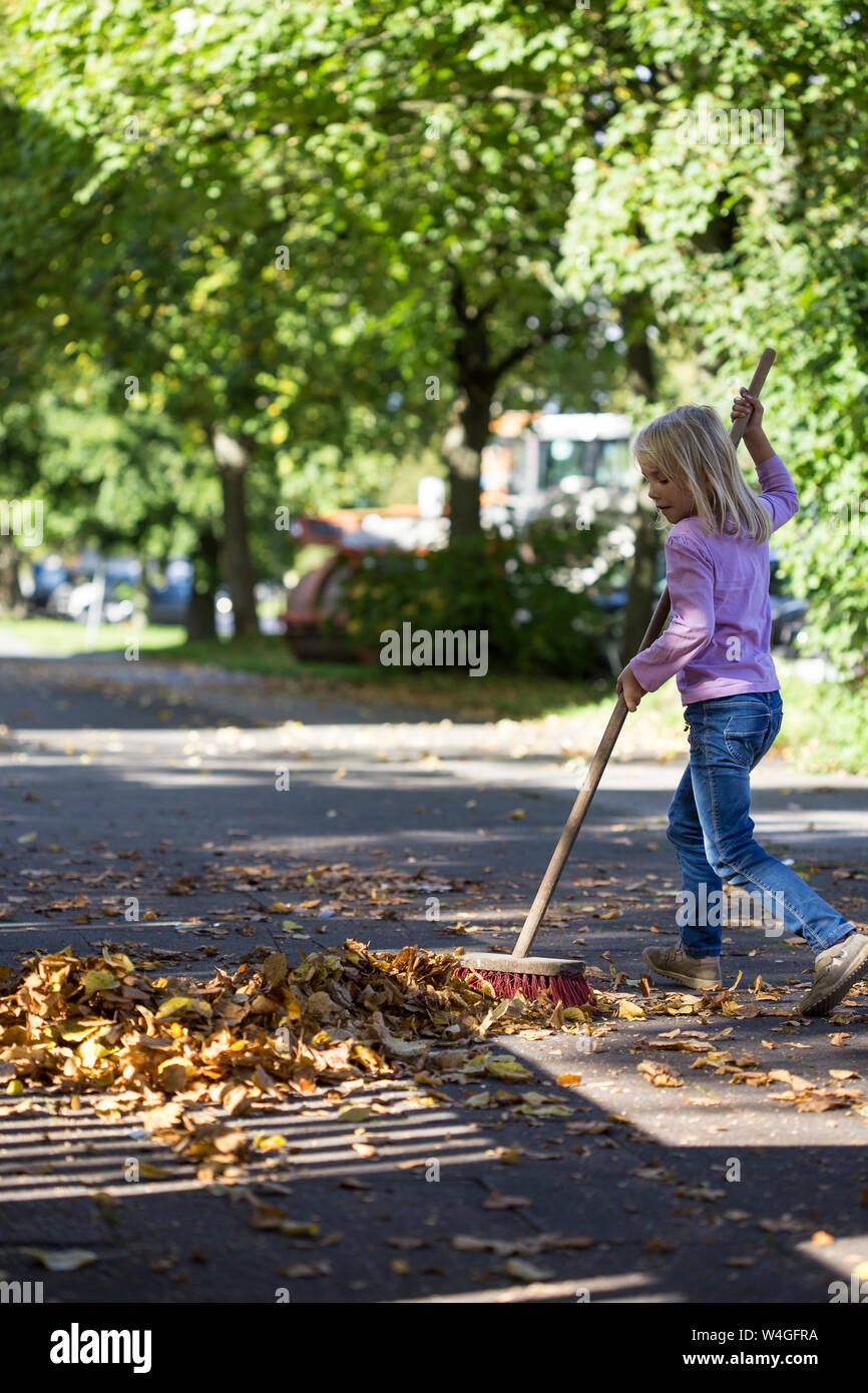 Mädchen fegt Blätter auf Pflaster Stockfoto
