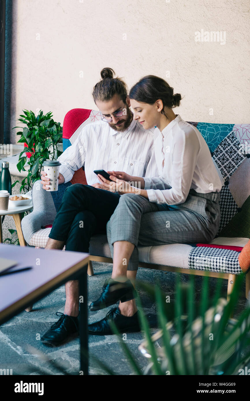 Junges Paar sitzt auf einem Sofa mit einem Smartphone Stockfoto