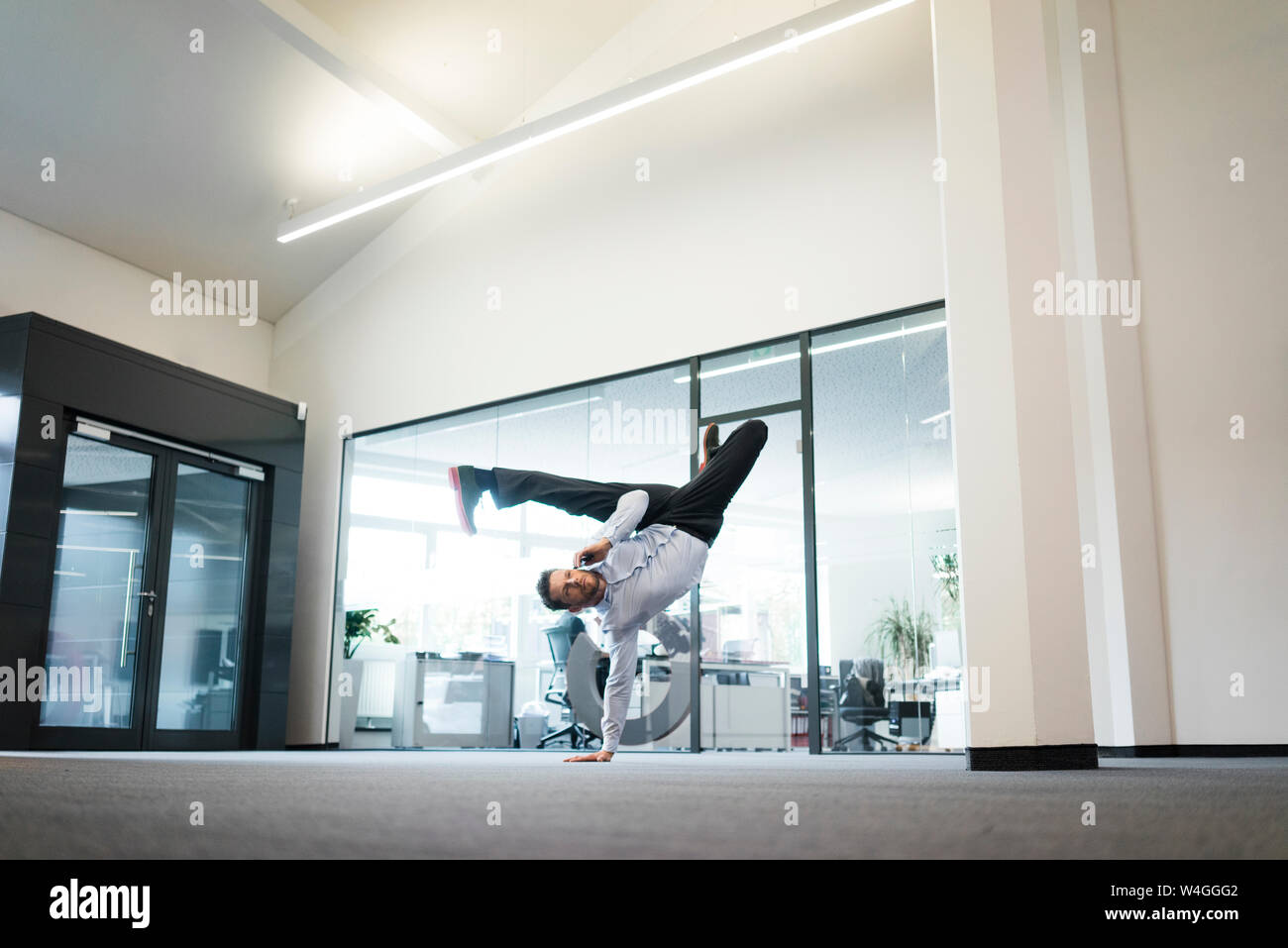 Geschäftsmann mit Mobiltelefon einen einhändigen Handstand auf Büro Etage Stockfoto