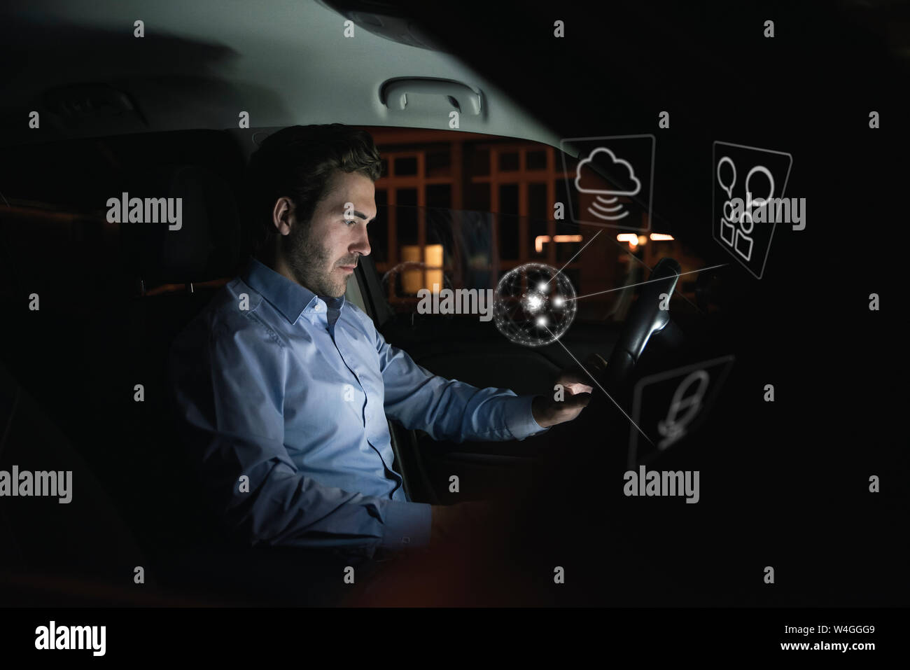 Geschäftsmann mit Gerät im Auto in der Nacht von Internet Symbolen umgeben Stockfoto