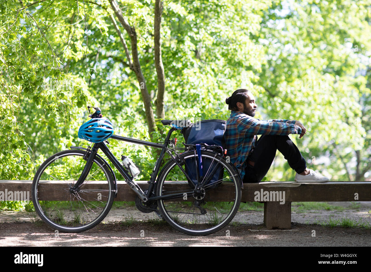 Junger Mann mit Fahrrad entspannend auf einer Bank Stockfoto