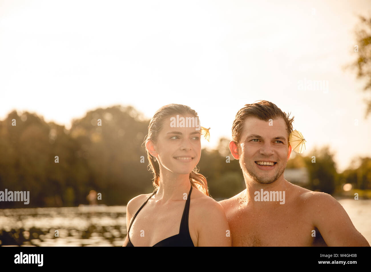 Junges Paar mit Getränk Sonnenschirme in ihrem Haar, Spaß am See Stockfoto