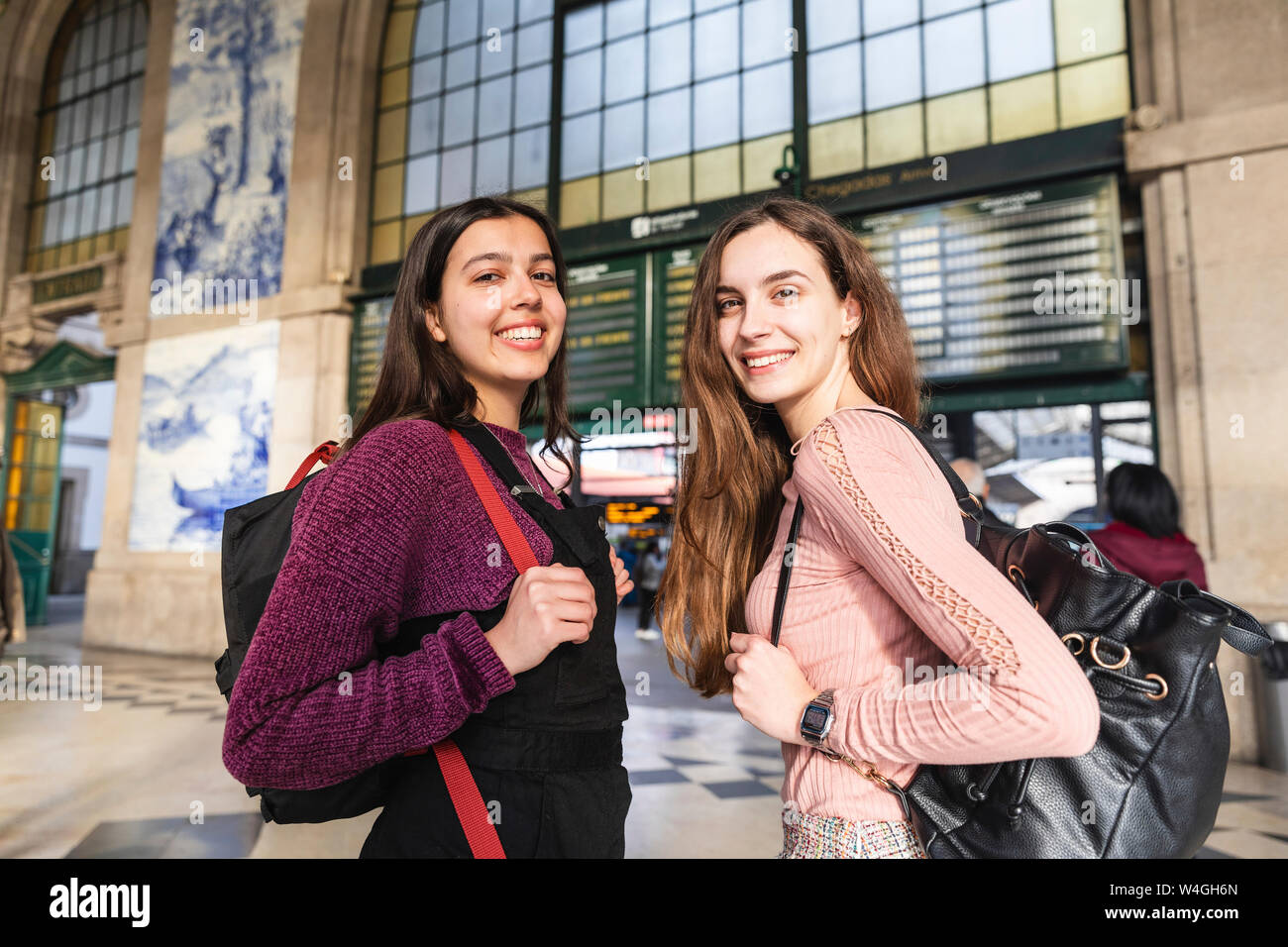 Portrait von zwei lächelnde junge Frauen mit Rucksäcken vor dem Bahnhof stehend, Porto, Portugal Stockfoto