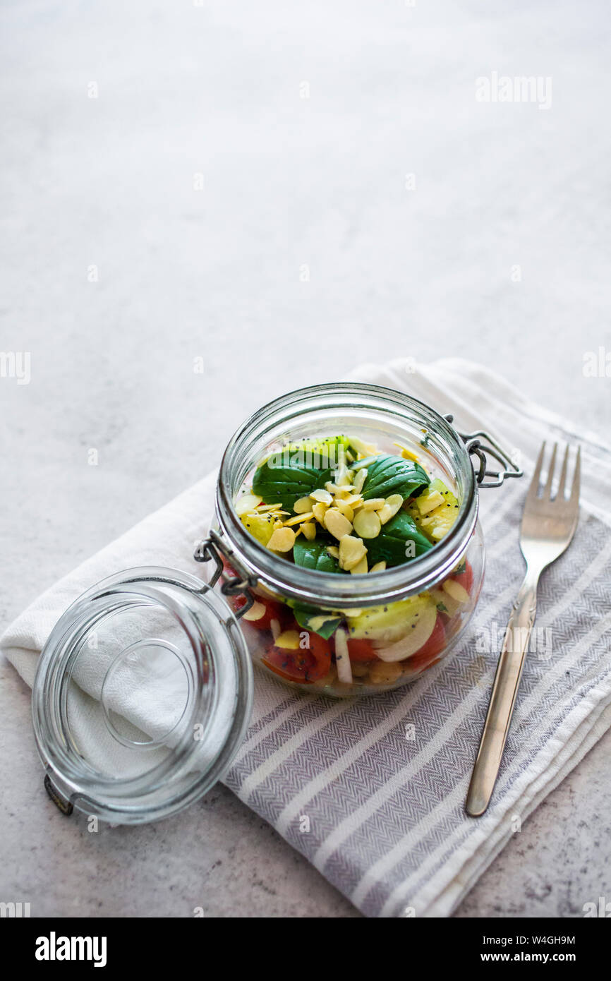 Glas Salat mit Gurken, Kichererbsen, Zwiebeln, Tomaten, Basilikum, Chia Samen und gehobelten Mandeln Stockfoto