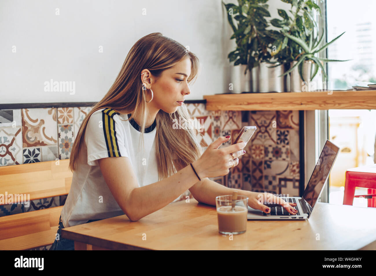 Junge Frau mit dem Handy und dem Laptop im Cafe Stockfoto