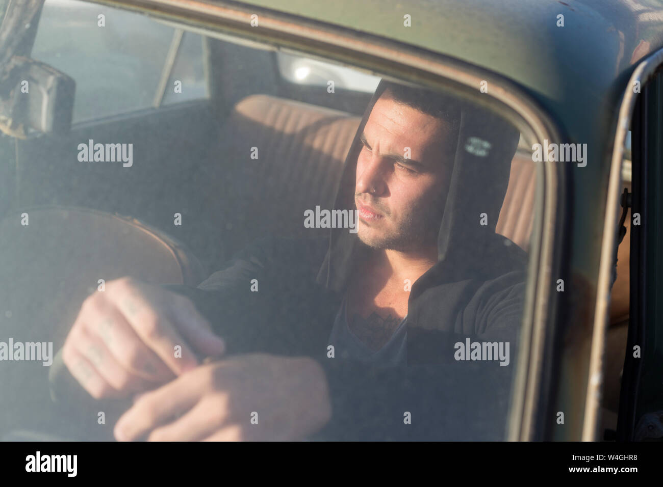 Junge Mann in einem defekten Auto sitzen auf einem Schrottplatz Stockfoto