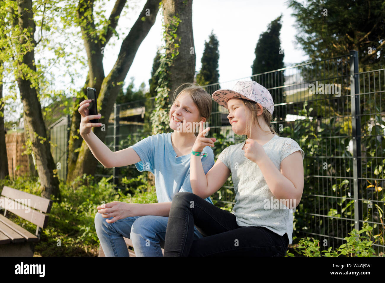 Zwei glückliche Mädchen sitzen auf einer Parkbank ein selfie Stockfoto