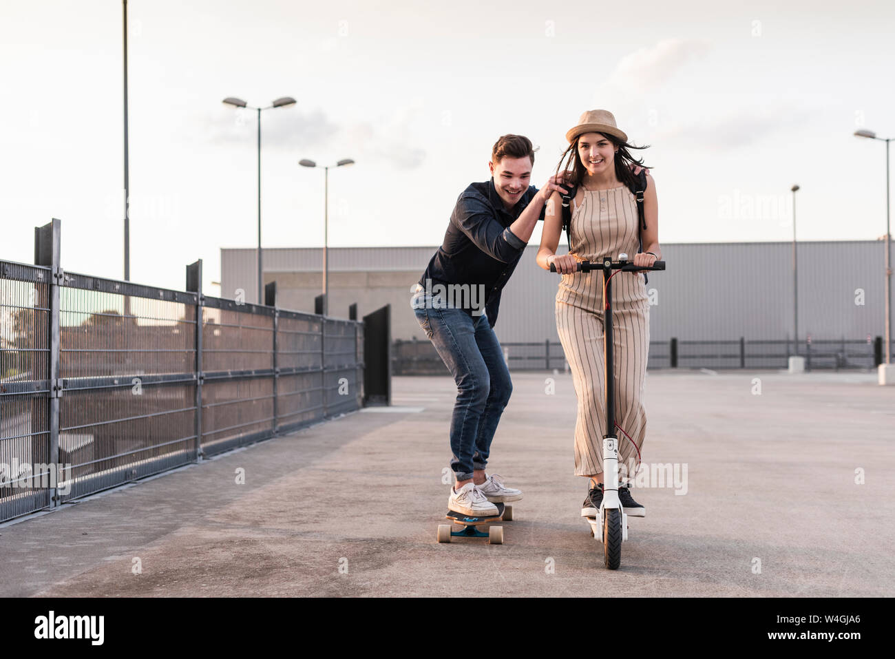 Junger Mann und eine Frau reiten auf Longboard und Elektroroller auf Parkdeck Stockfoto