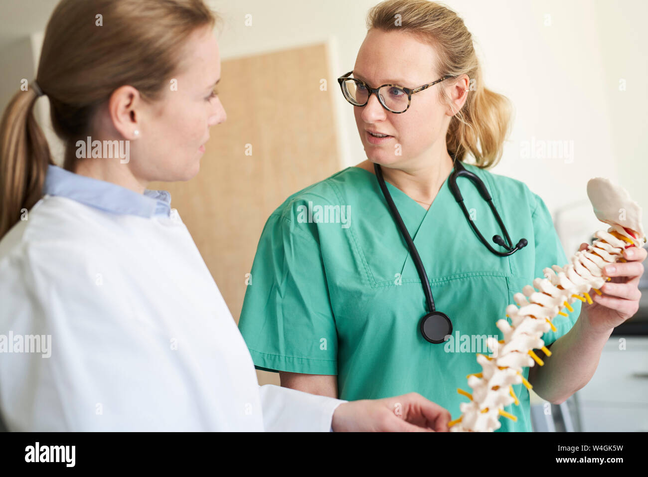 Ärztin und Frau in Scrubs mit wirbelsäule Modell sprechen Stockfoto