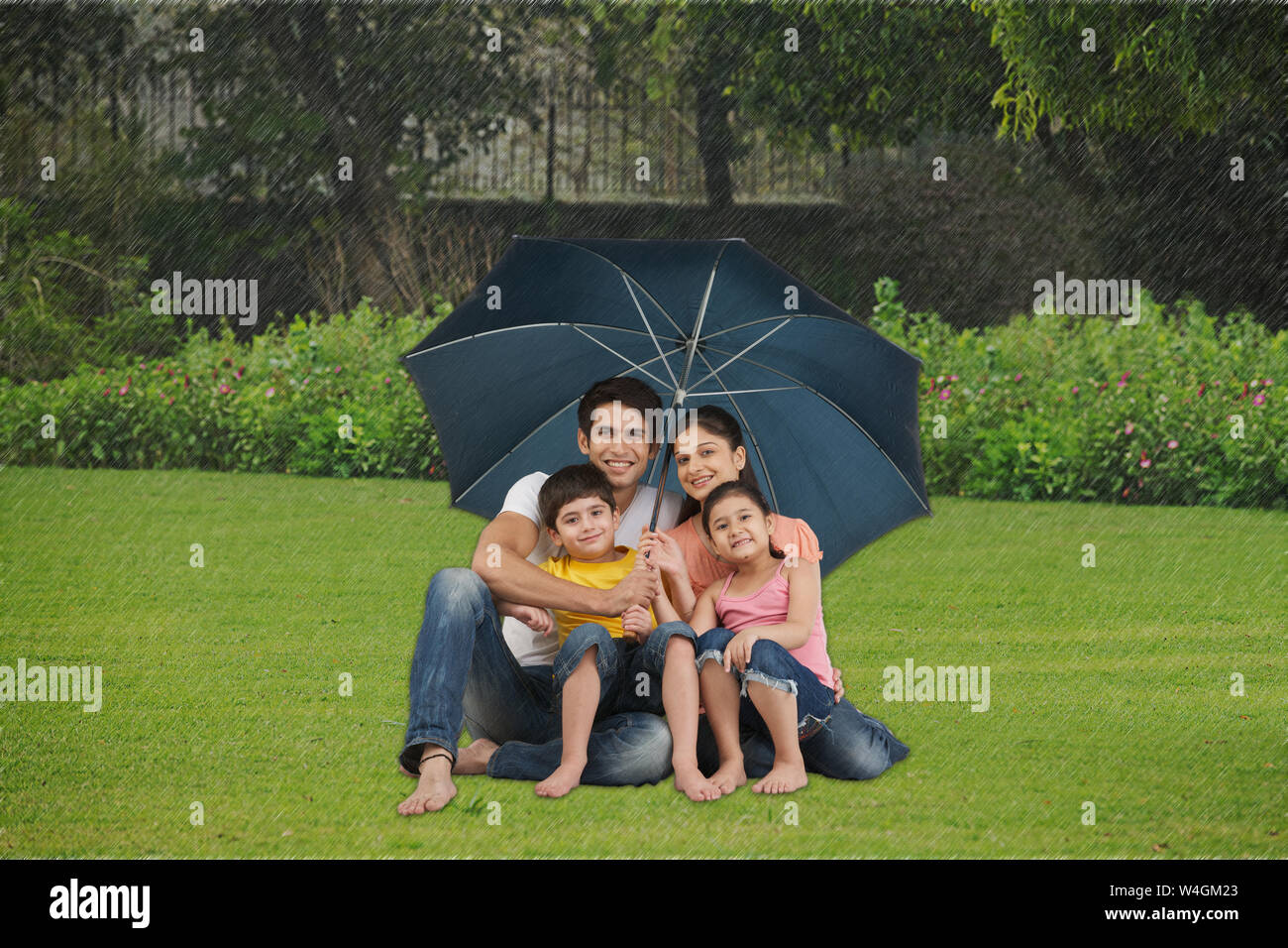 Familie sitzt unter einem Sonnenschirm auf einem Rasen Stockfoto
