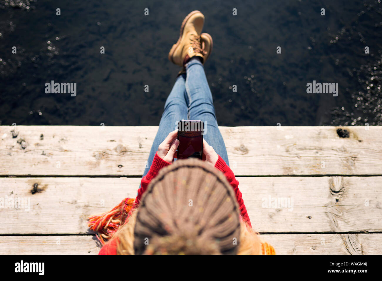 Junge blonde Frau mit Smartphone an einem See im Winter Stockfoto