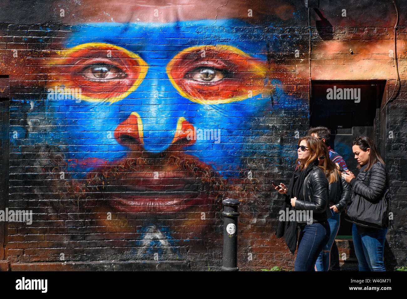 Leute, die durch die Graffiti wall Kunst an der Brick Lane Market in London, Vereinigtes Königreich Stockfoto