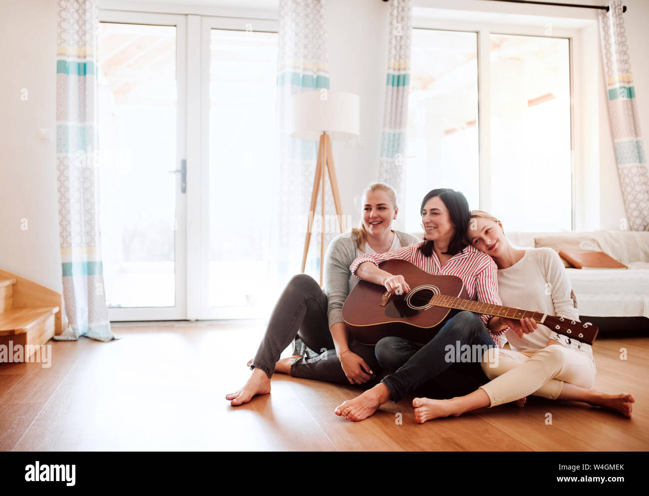 Reife Frau mit zwei Töchtern auf dem Boden Gitarre spielen zu Hause sitzen Stockfoto