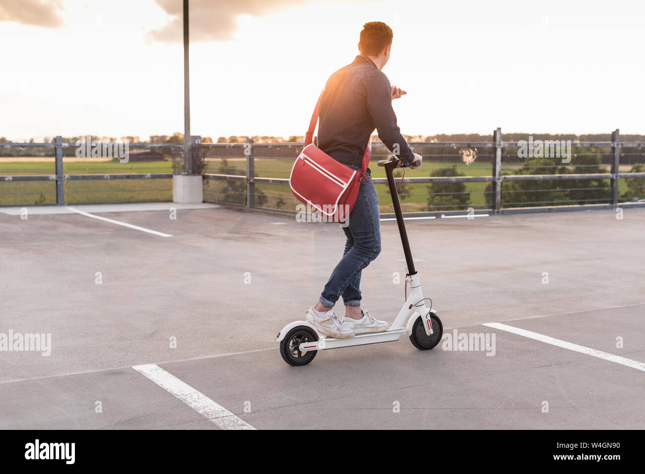 Junger Mann mit Handy und Elektroroller auf Parkdeck bei Sonnenuntergang Stockfoto