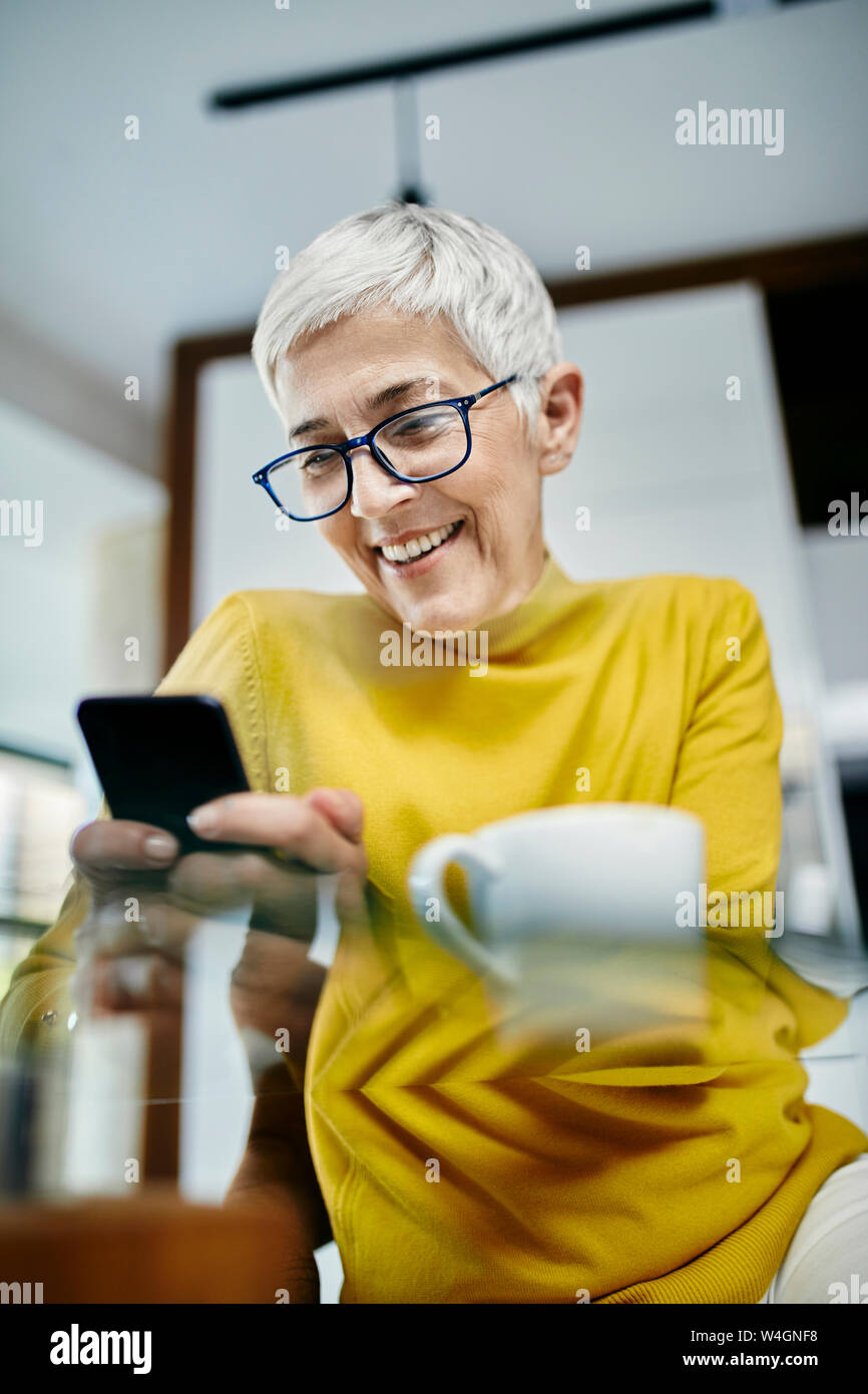 Ältere Frau trinkt Kaffee, Kontrolle SMS-Nachrichten auf Ihrem Smartphone Stockfoto