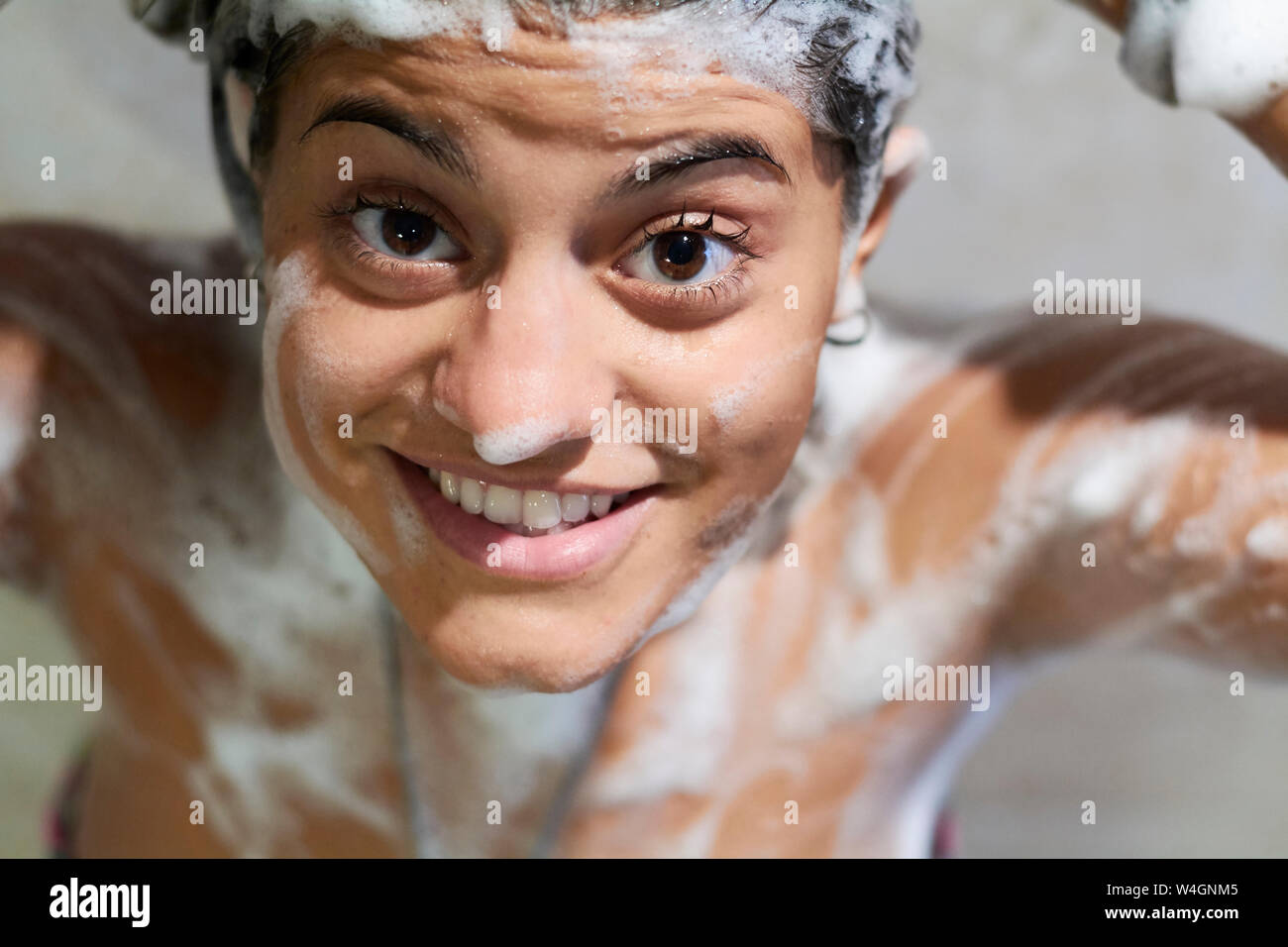 Lächelnde junge Frau mit Seife auf Body Dusche, an Kamera suchen Stockfoto