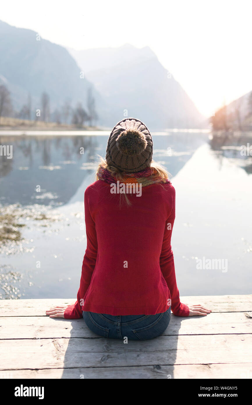 Blonde junge Frau sitzt auf der Jetty an einem See im Winter Stockfoto