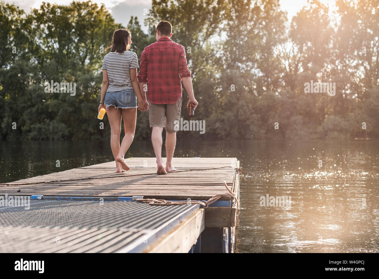 Junges Paar Hand in Hand auf Steg an einem entfernten See Stockfoto