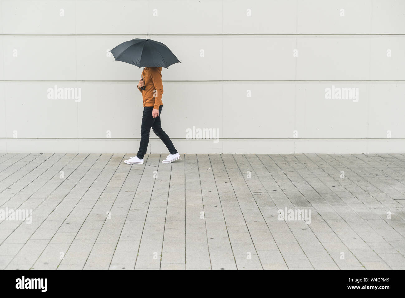 Junger Mann mit Schirm zu Fuß auf der Straße Stockfoto