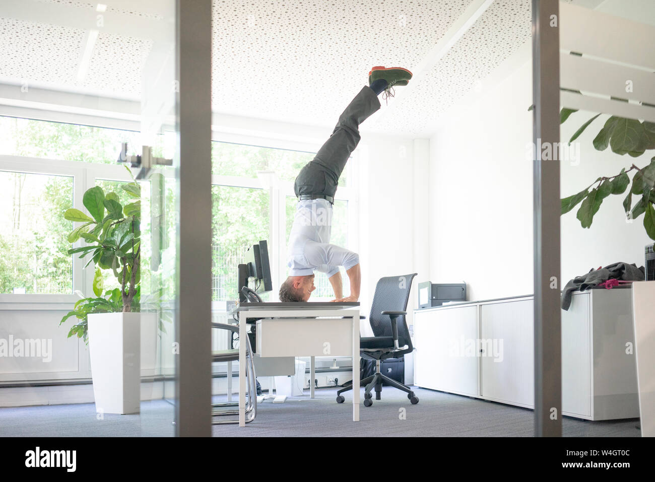 Unternehmer tun ein Kopfstand auf dem Schreibtisch im Büro Stockfoto