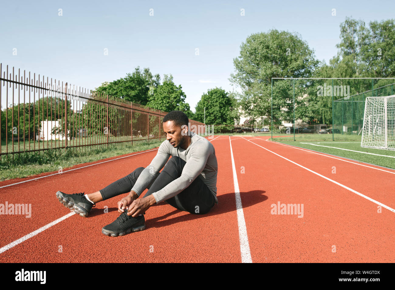 Sportler sitzen auf Rennstrecke und binden Schuhe vor dem Training Stockfoto