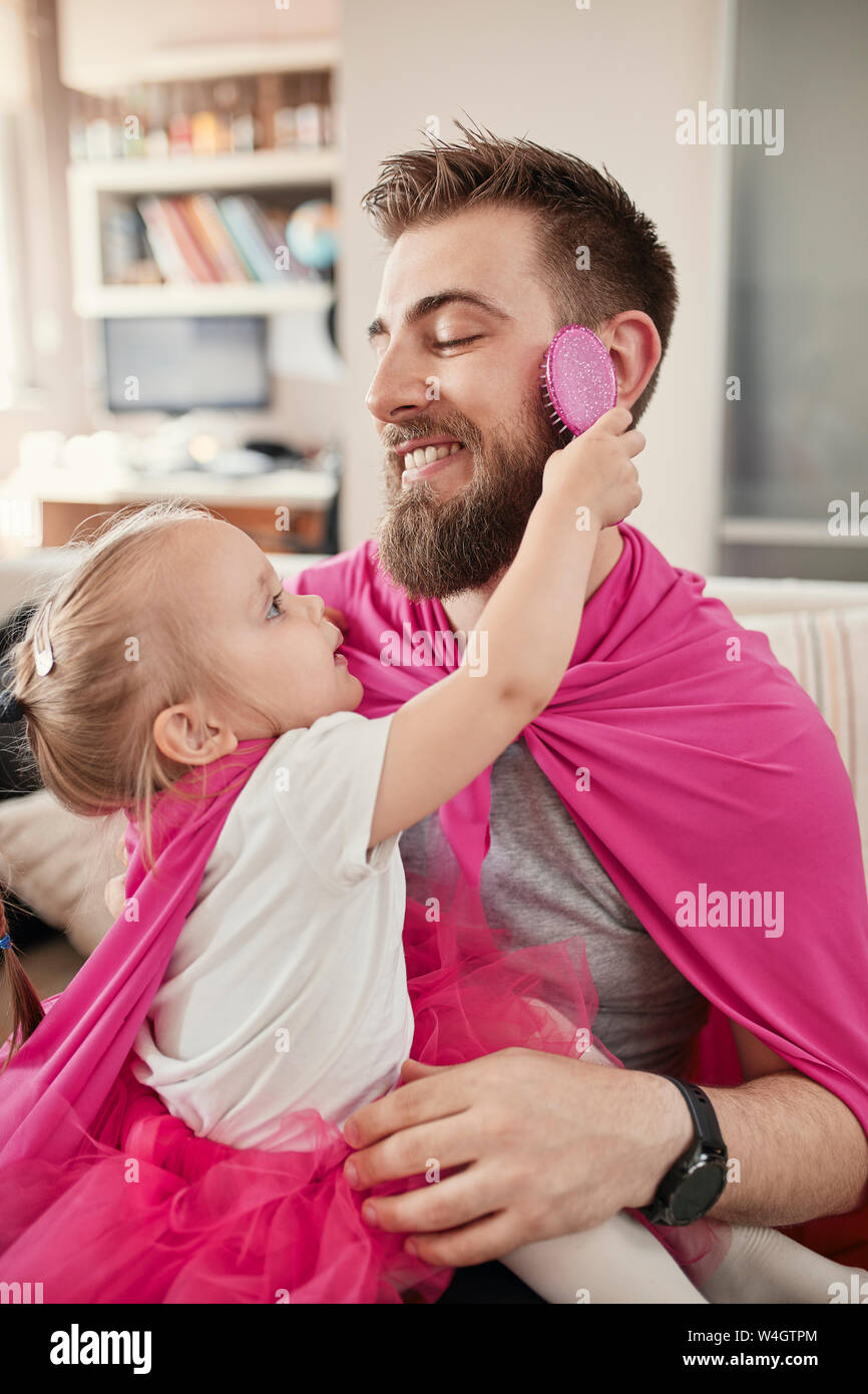 Vater und Tochter spielen Superhelden und superwoman, Mädchen bürsten Bart Stockfoto