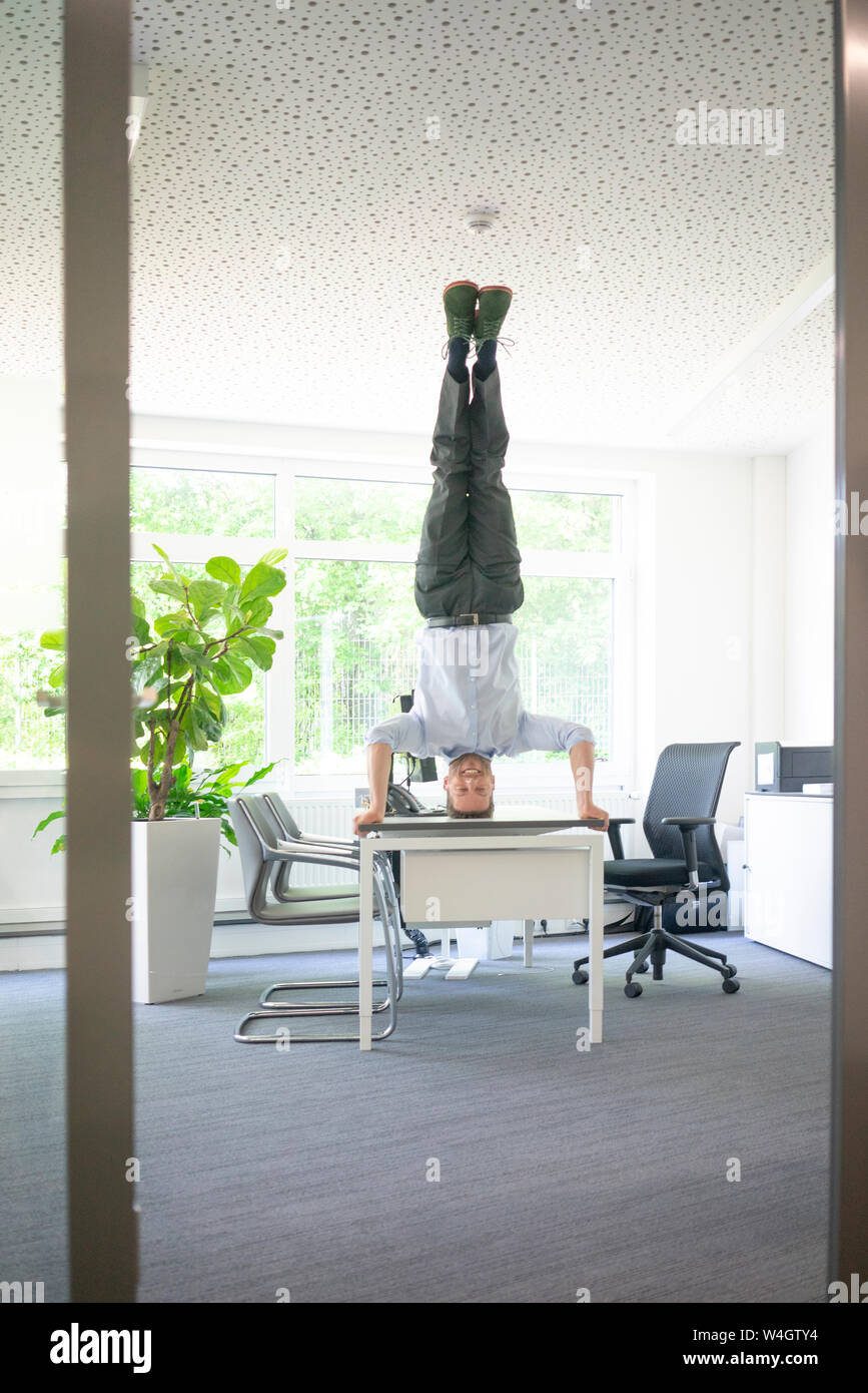 Unternehmer tun ein Kopfstand auf dem Schreibtisch im Büro Stockfoto