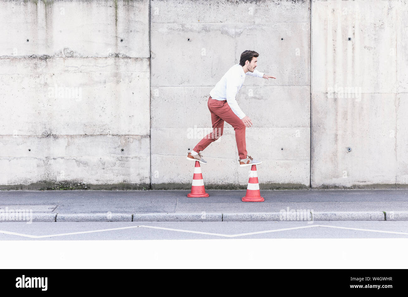 Junger Mann Balancieren auf leitkegel vor betonwand Stockfoto