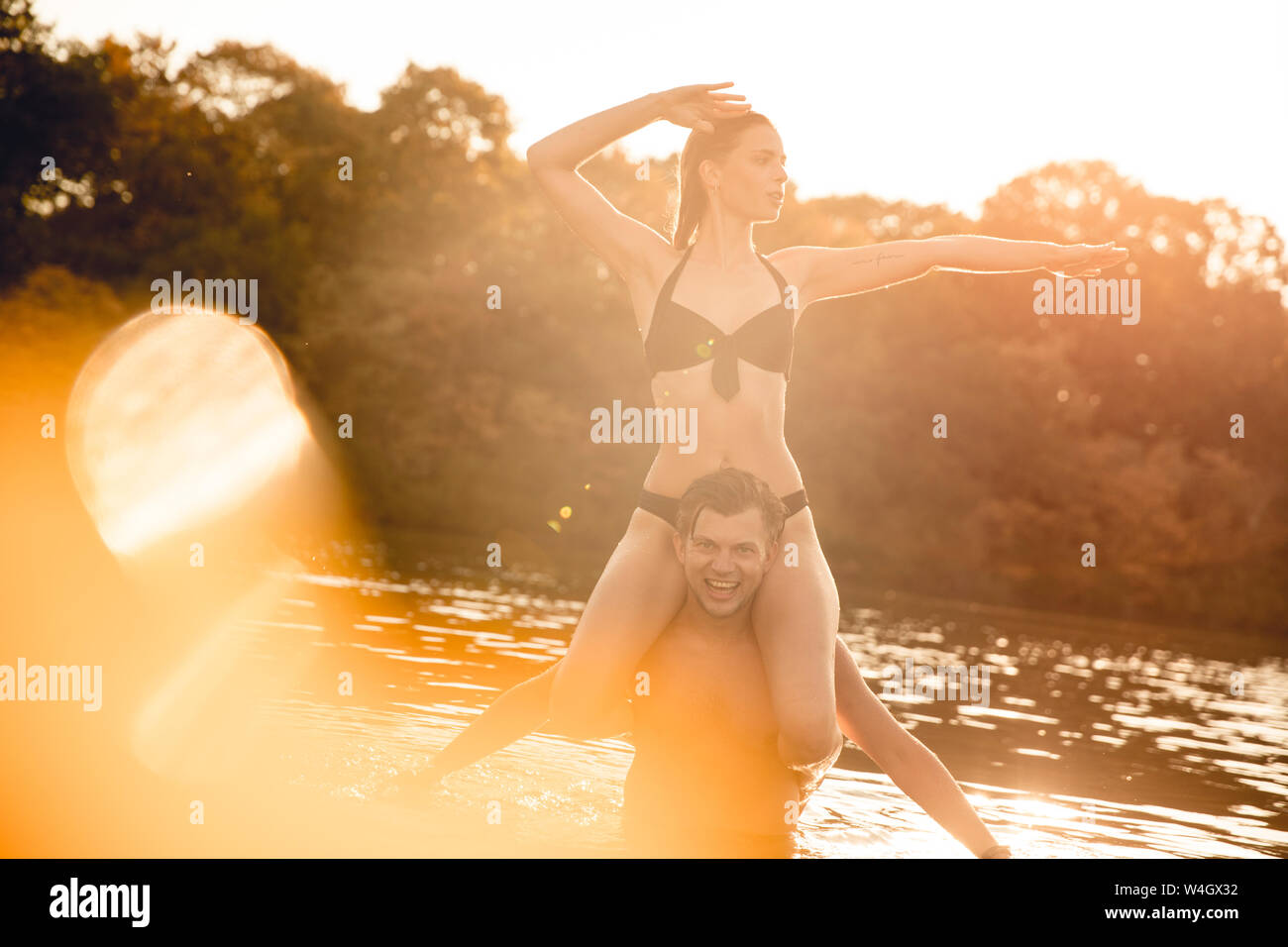 Junge Frau sitzt auf den Schultern der jungen Mann in See, um in der Sonne Stockfoto