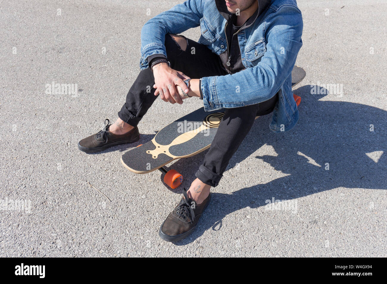 Tätowierte junge Mann sitzt auf Longboard, Teilansicht Stockfoto