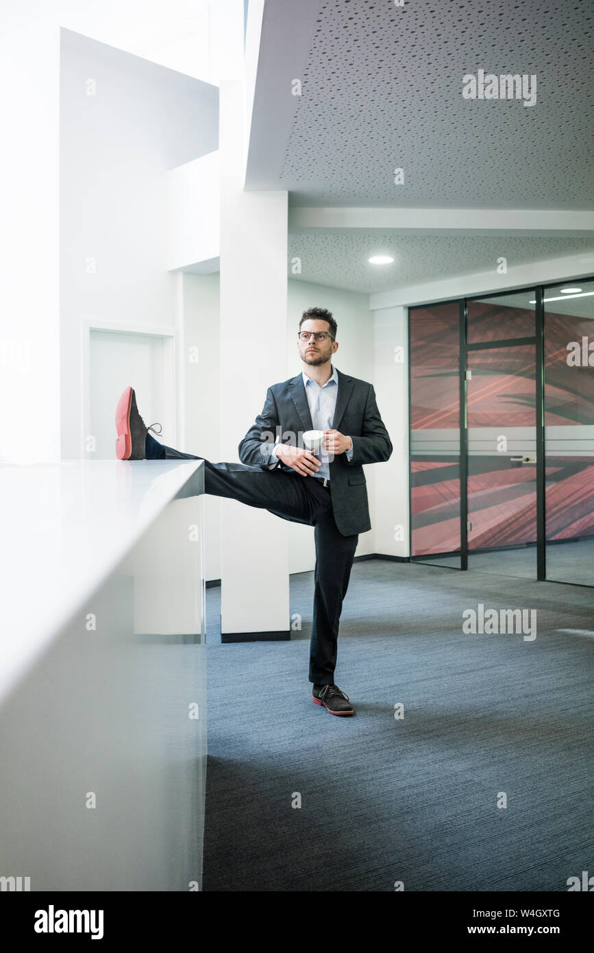 Geschäftsmann mit Tasse Kaffee stehen auf einem Bein im Büro Stockfoto