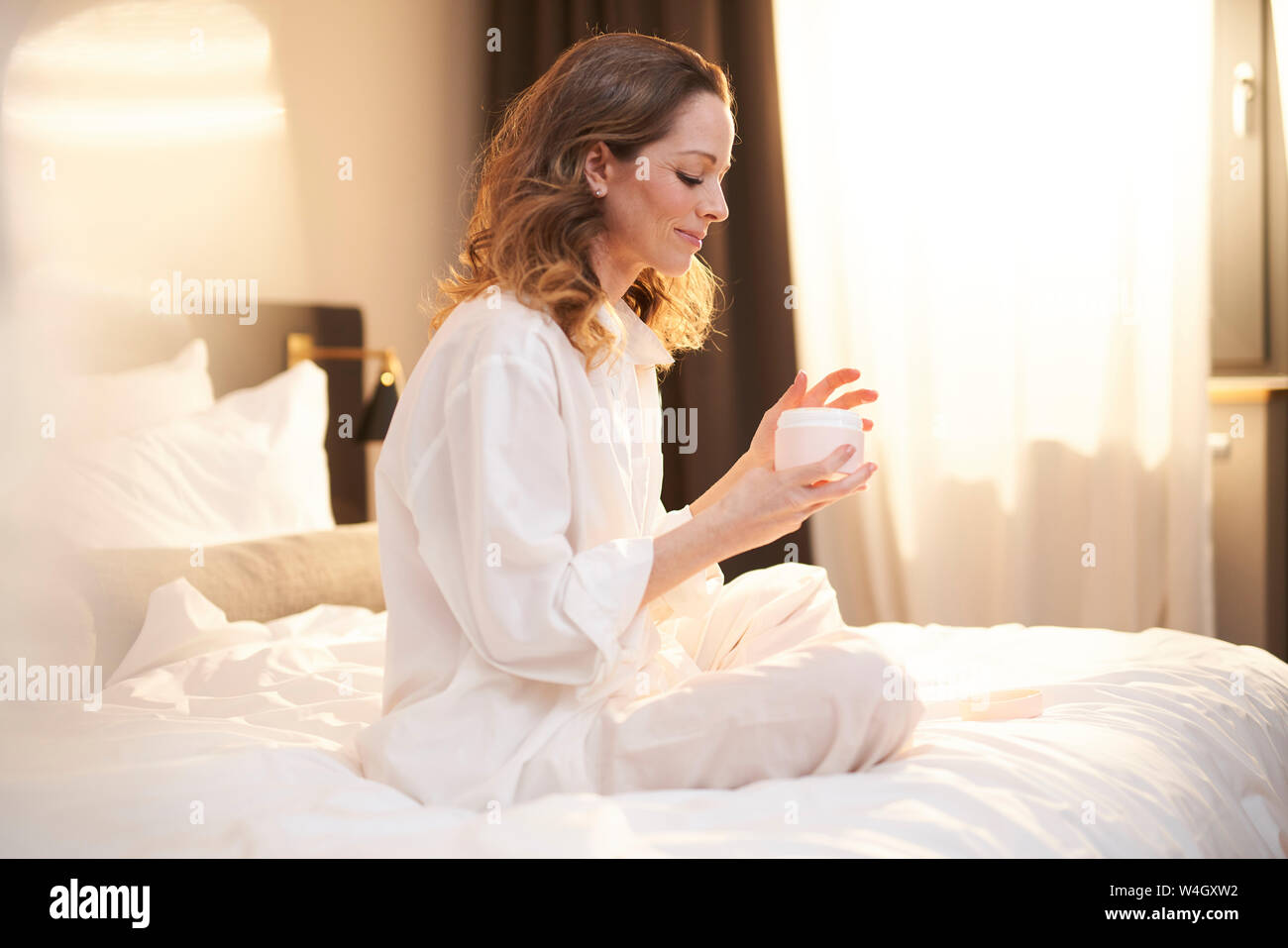 Brünette Frau sitzt auf dem Bett, die Schönheit Creme Stockfoto