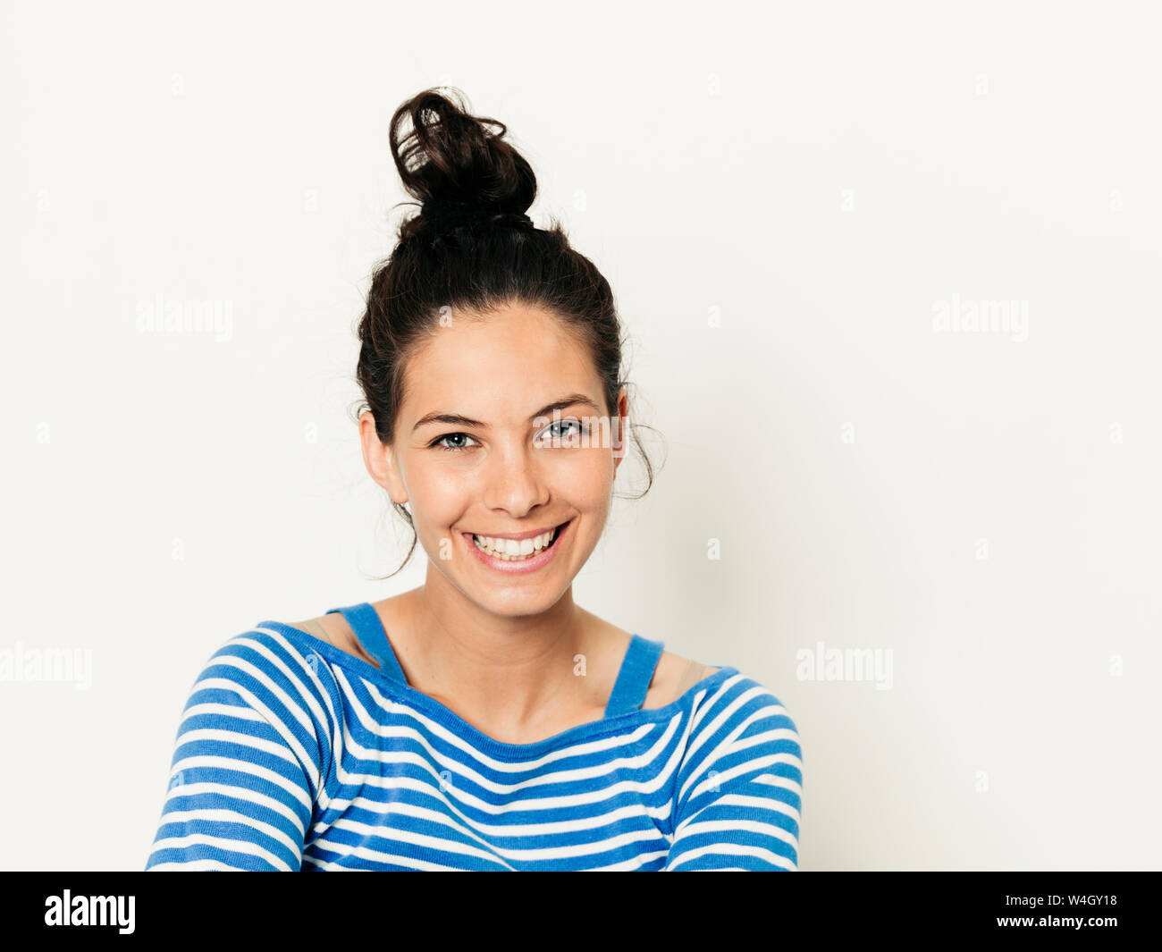 Schöne junge Frau mit schwarzen Haaren und blau-weiß gestreiften Pullover ist vor weißem Hintergrund posiert Stockfoto