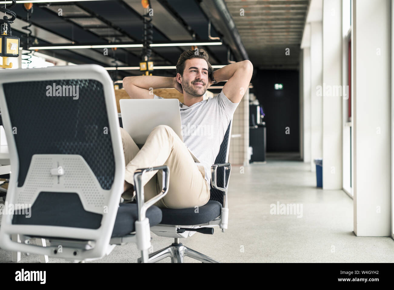 Junge Unternehmer arbeiten in modernen Büros entspannt, mit Laptop auf dem Schoß Stockfoto
