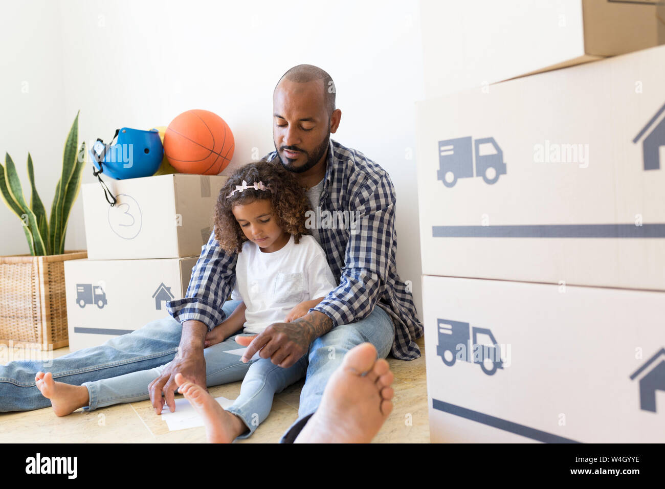 Vater und Tochter sitzen auf dem Boden im neuen Zuhause von Kartons umgeben Stockfoto