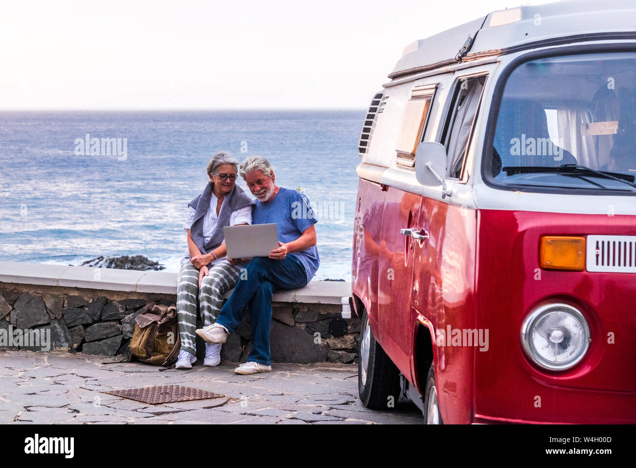 Senior Paar reist in einer vintage Van, mit Laptop, sitzen auf einer Mauer am Meer Stockfoto