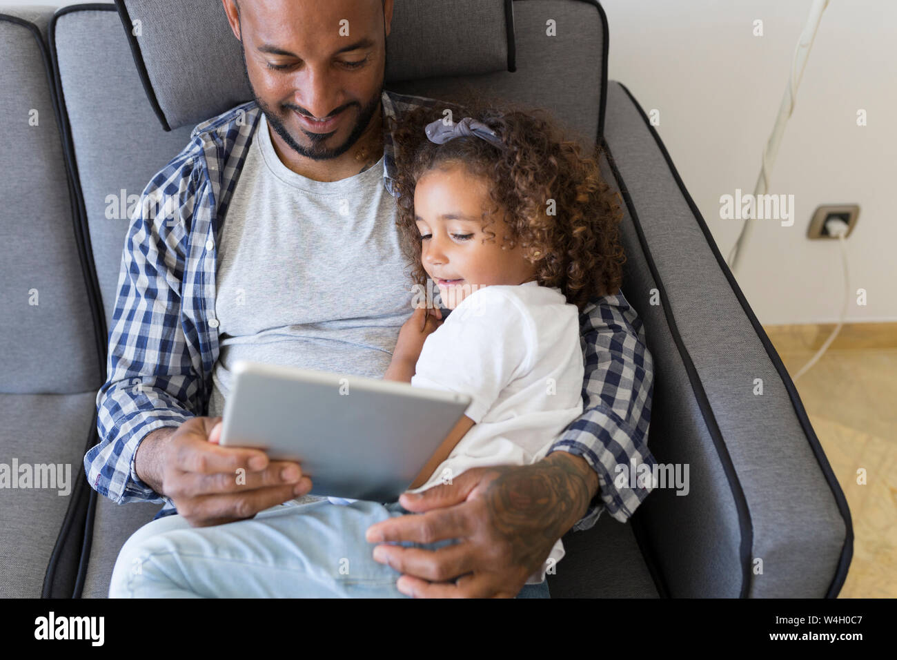 Vater und Tochter auf der Couch zu Hause sitzen zusammen an Tablet suchen Stockfoto