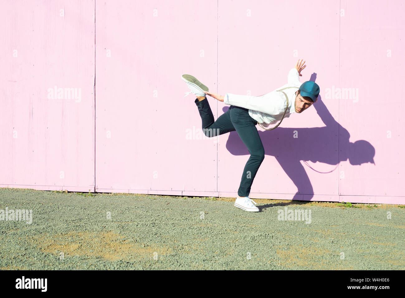 Junger Mann vor rosa Bau Barriere, auf ein Bein Stockfoto
