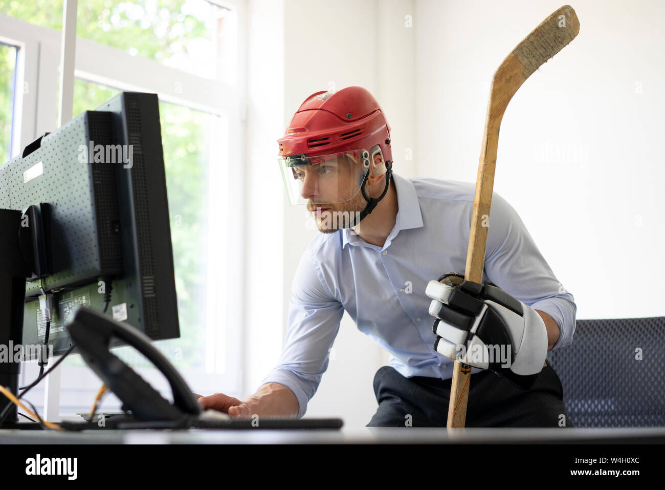 Kaufmann verkleidet als Eishockey Spieler am Schreibtisch im Büro arbeiten Stockfoto