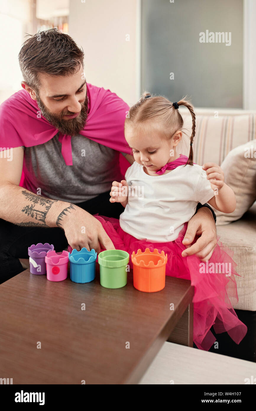 Vater und Tochter tragen Superhelden und superwoman Kostüm, spielen mit Stapeln von Cups Stockfoto