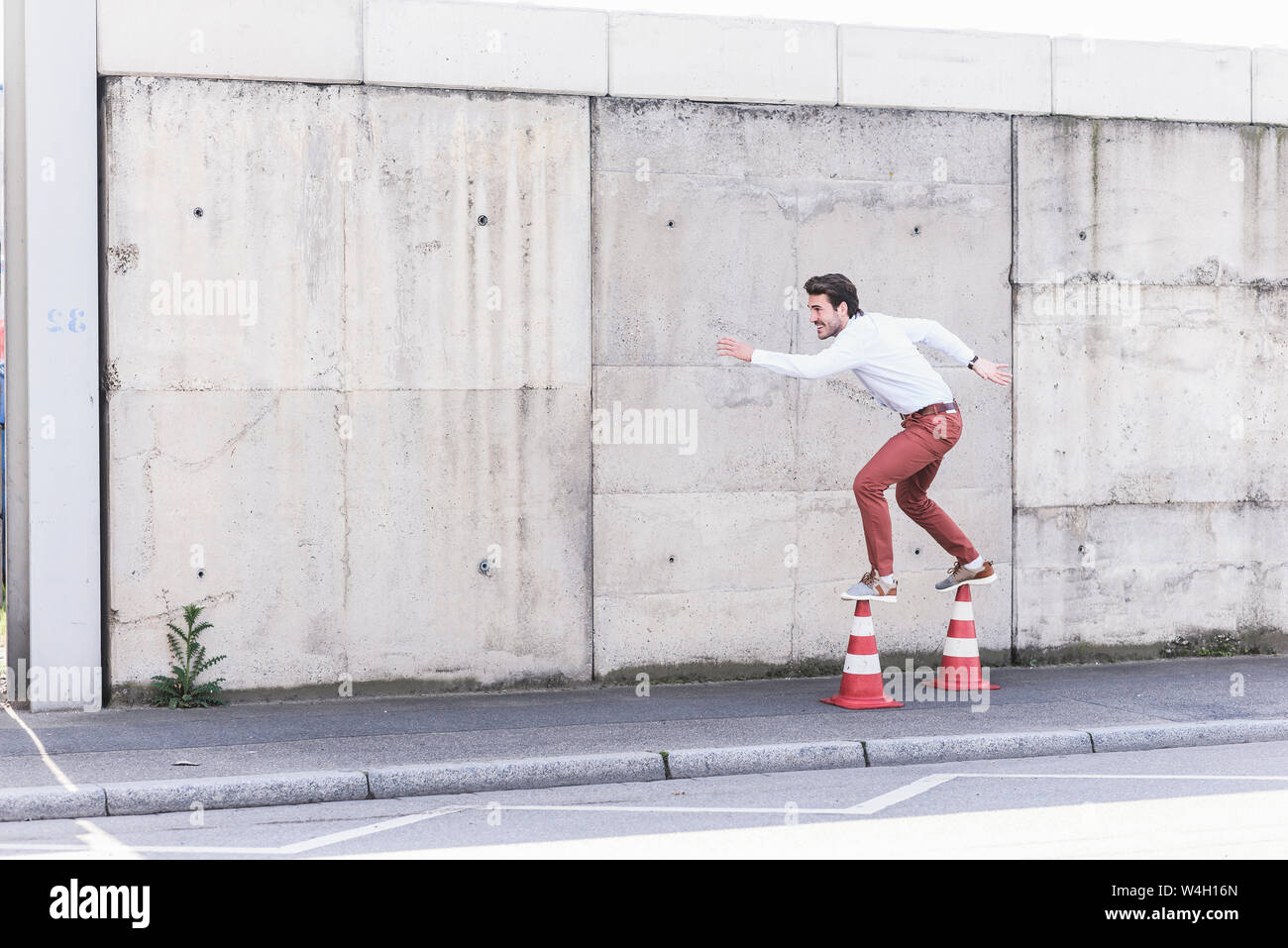 Junger Mann Balancieren auf leitkegel vor betonwand Stockfoto