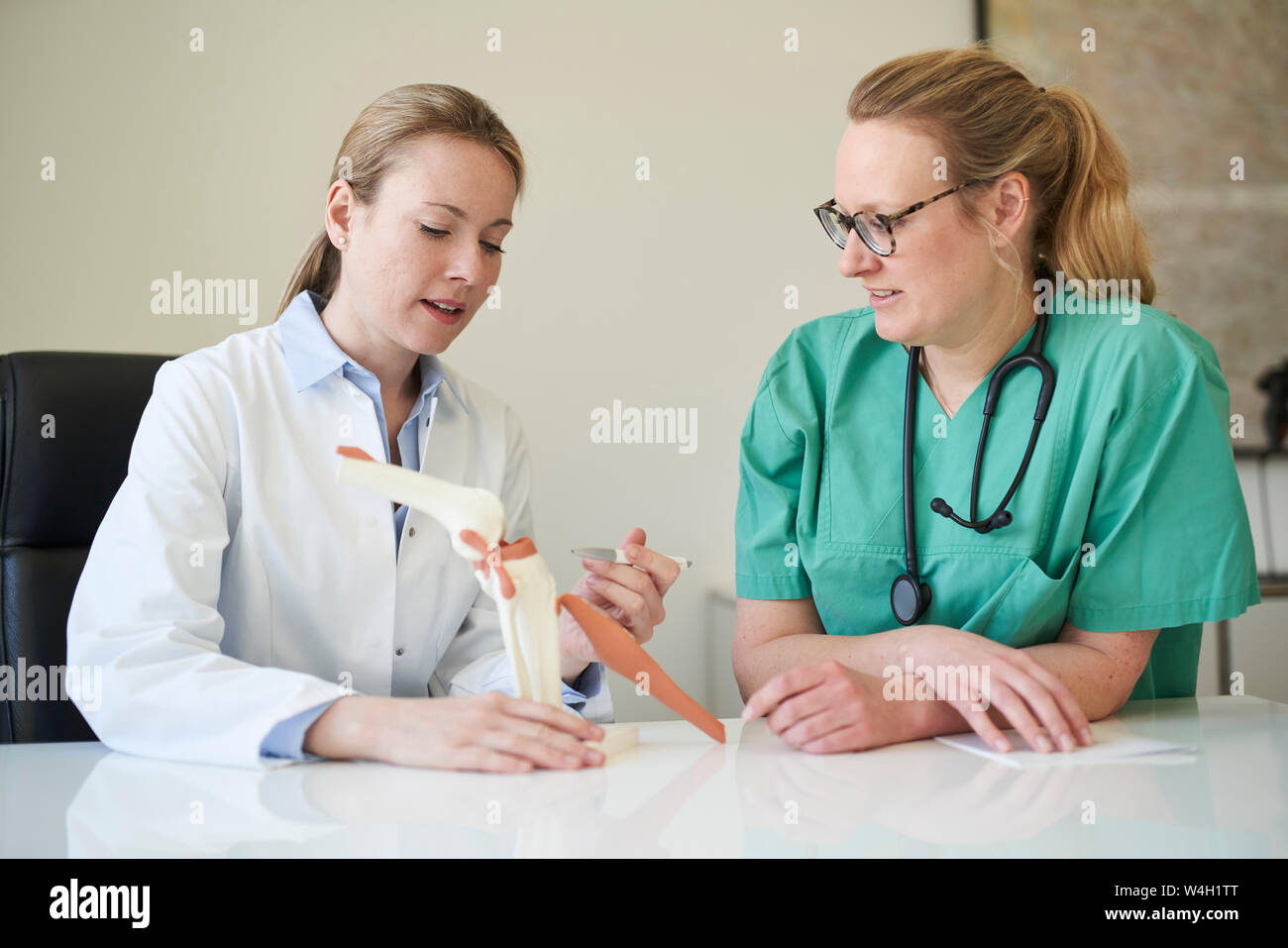 Ärztin und Frau in Scrubs mit kniegelenk Modell sprechen Stockfoto