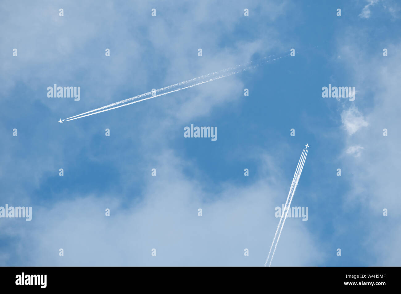 Zwei Flugzeuge überqueren Sie die blauen bewölkten Himmel in entgegengesetzte Richtungen in großer Höhe fliegenden Stockfoto