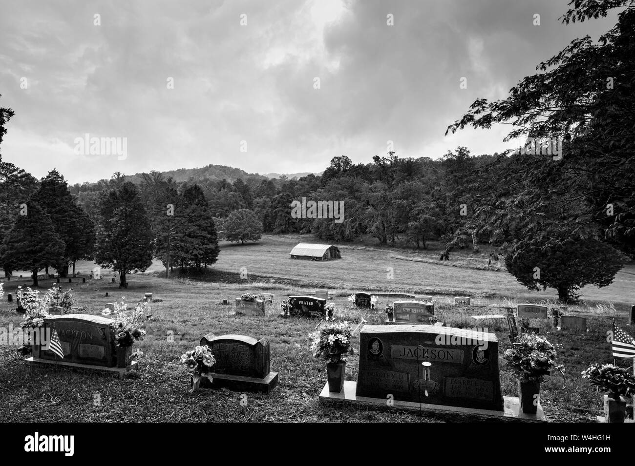 Die Entwicklung des ländlichen Friedhofs und Grabsteine mit Blick auf Land Scheune in Eastern Tennessee Appalachian Berge der USA in Schwarz und Weiß Stockfoto