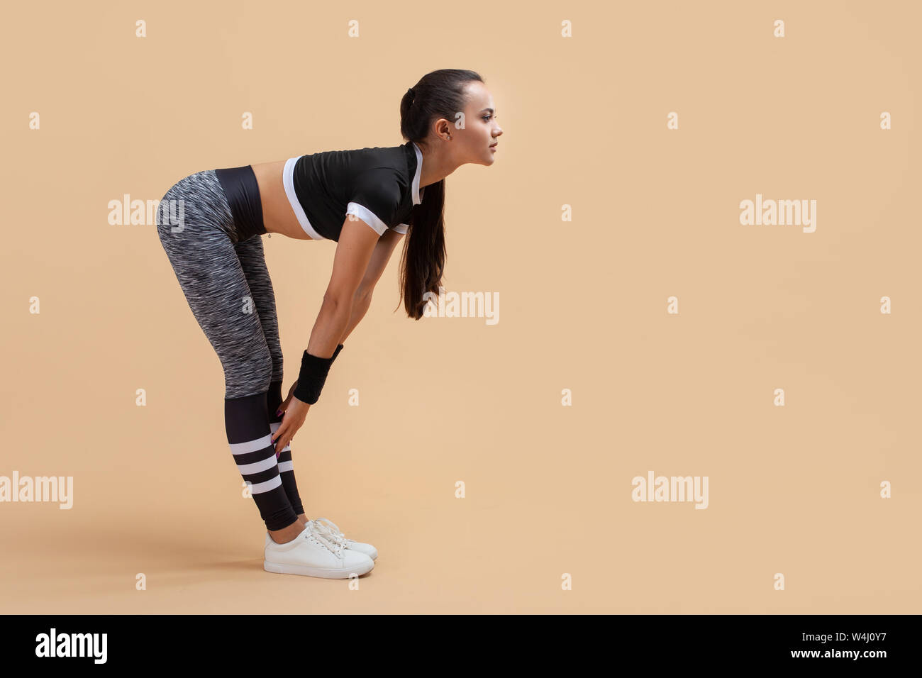 Ein junges attraktives Mädchen, Brünette mit einem Schwanz und in langen grauen Leggings, biegt sich nach vorn, recken ihre Arme gegen einen Pfirsich Hintergrund. Kopieren Sie Platz. Stockfoto