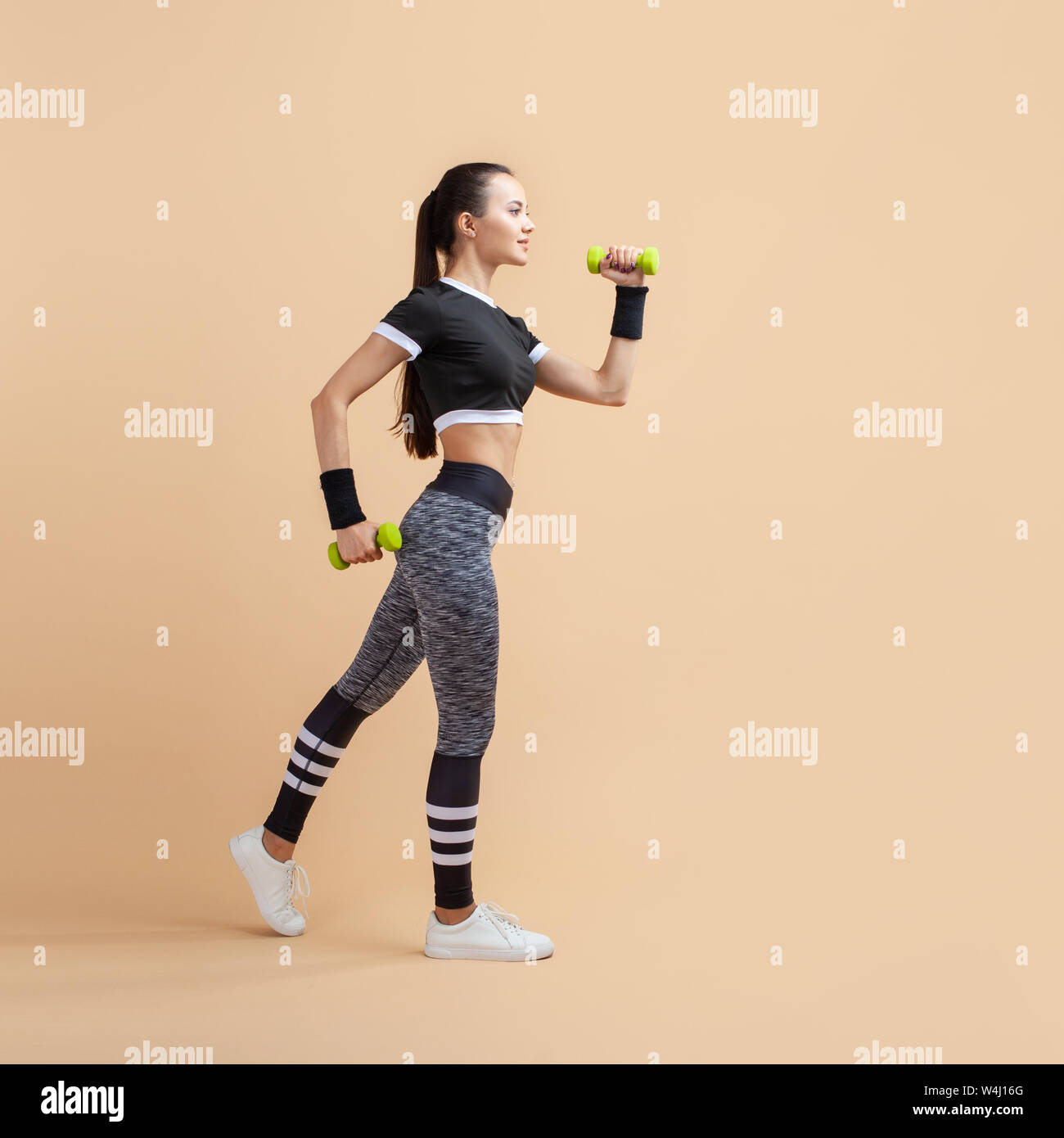 Ein junges Mädchen, Brünette mit einem Pferdeschwanz und in langen grauen Leggings, springt auf und ab mit grünen Hanteln in den Händen. Stockfoto