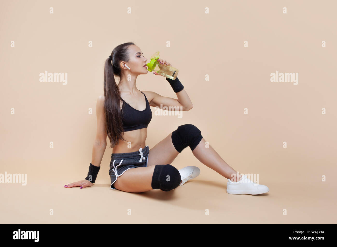 Ein niedliches athletische brunette Mädchen, in einer enganliegenden Sport einheitliche, sitzt, liegt nach dem Training, in schwarz Kniescheiben, mit einer Flasche für Sporternährung. Stockfoto