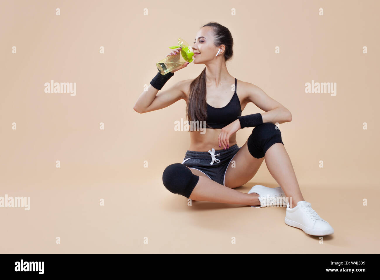 Ein niedliches athletische brunette Mädchen, in einer enganliegenden Sport einheitliche, sitzt, liegt nach dem Training, in schwarz Kniescheiben, mit einer Flasche für Sporternährung. Stockfoto