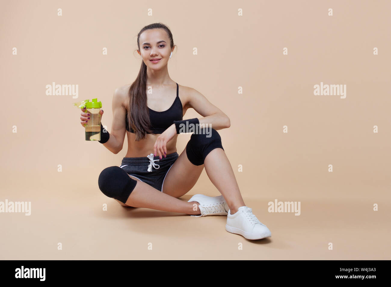Ein niedliches athletische brunette Mädchen, in einer enganliegenden Sport einheitliche, sitzt, liegt nach dem Training, in schwarz Kniescheiben, mit einer Flasche für Sporternährung. Stockfoto
